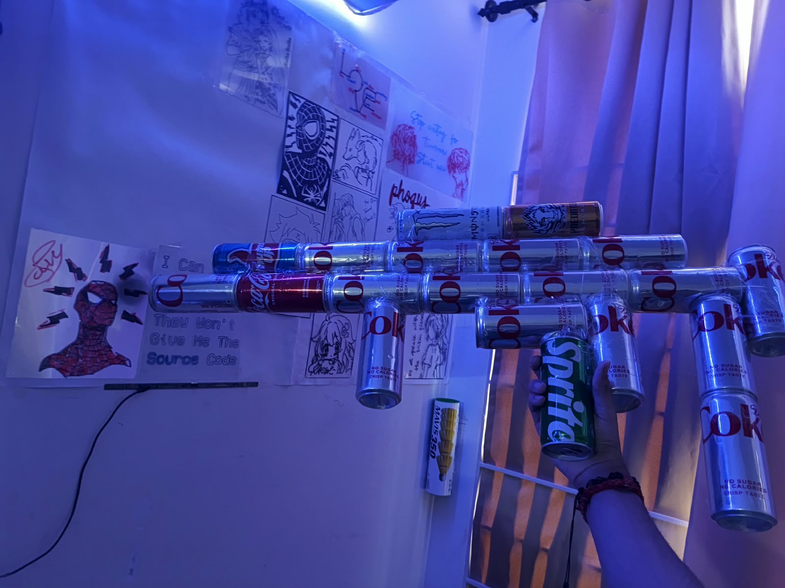 A handmade sculpture assembled from drink cans beside wall drawings in blue lighting